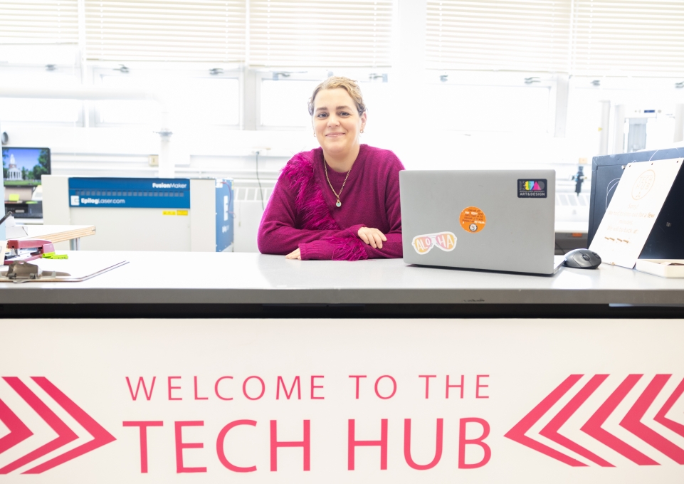 Jaclyn Ellis sits behind a desk with a sign that says welcome to the tech hub